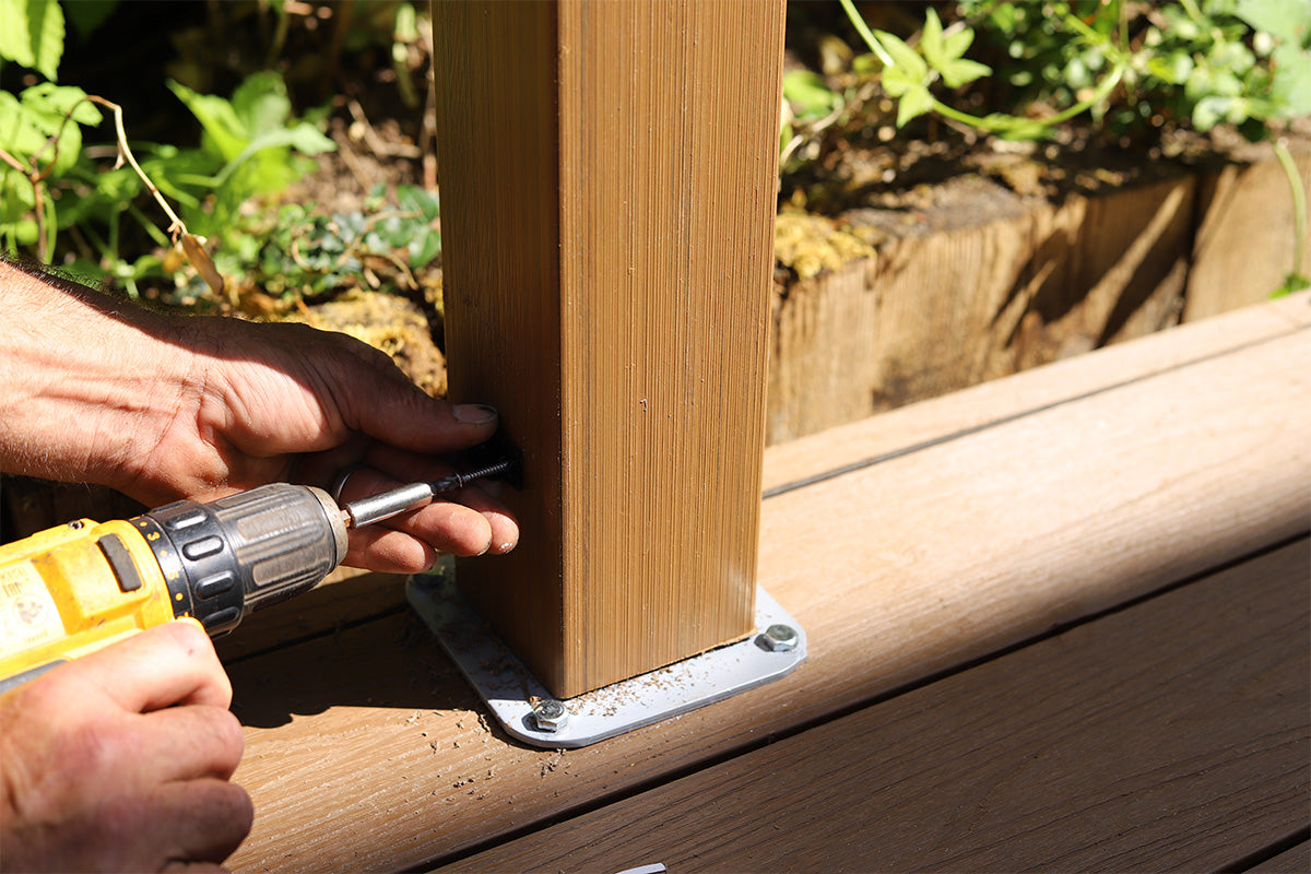 person using a drill to secure a composite balustrade post to a composite deck