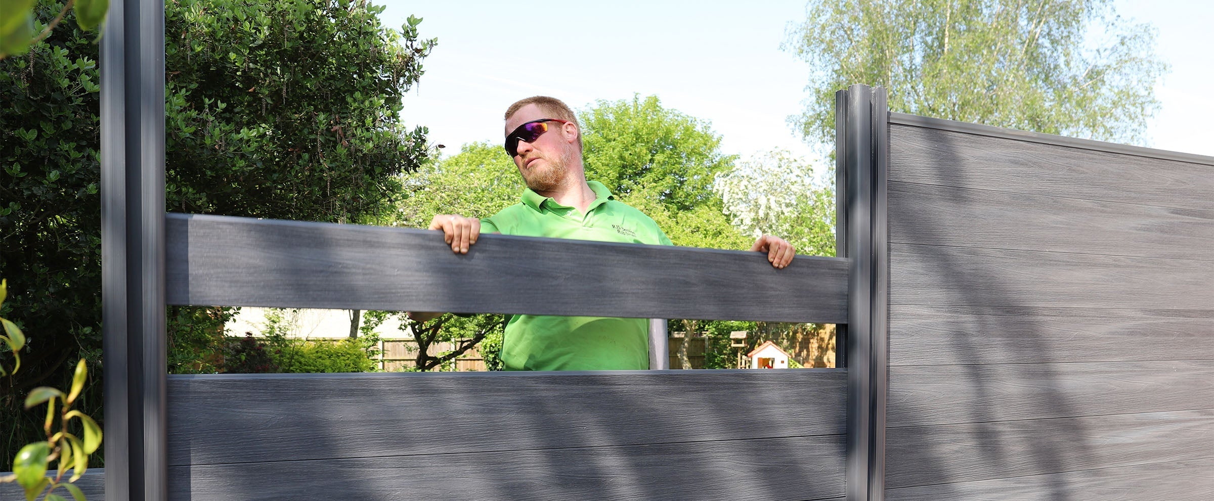 man installing a composite fence board into composite posts, with trees in the background