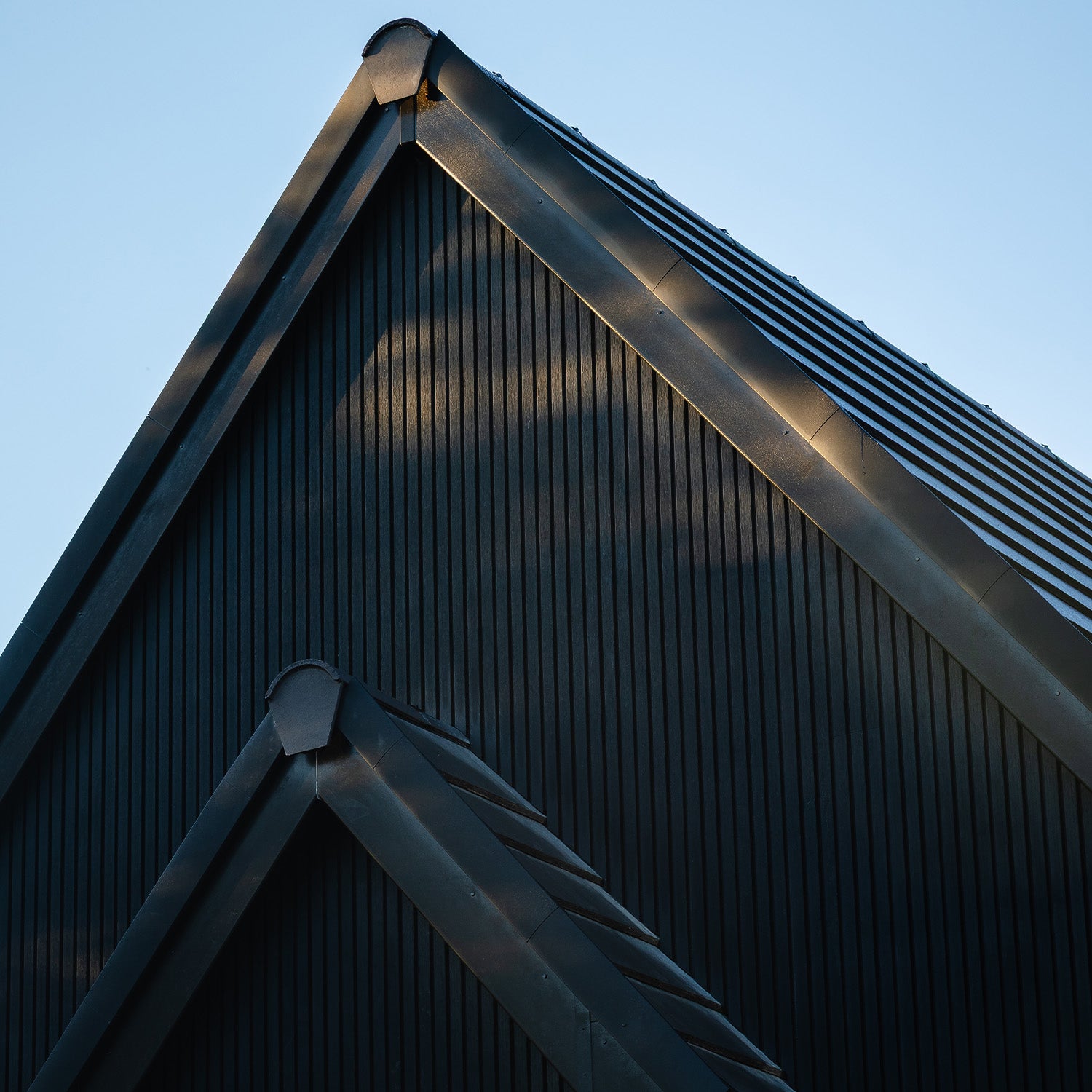 close-up of a dark metal roof, charcoal slatted composite cladding, with a clear blue sky background