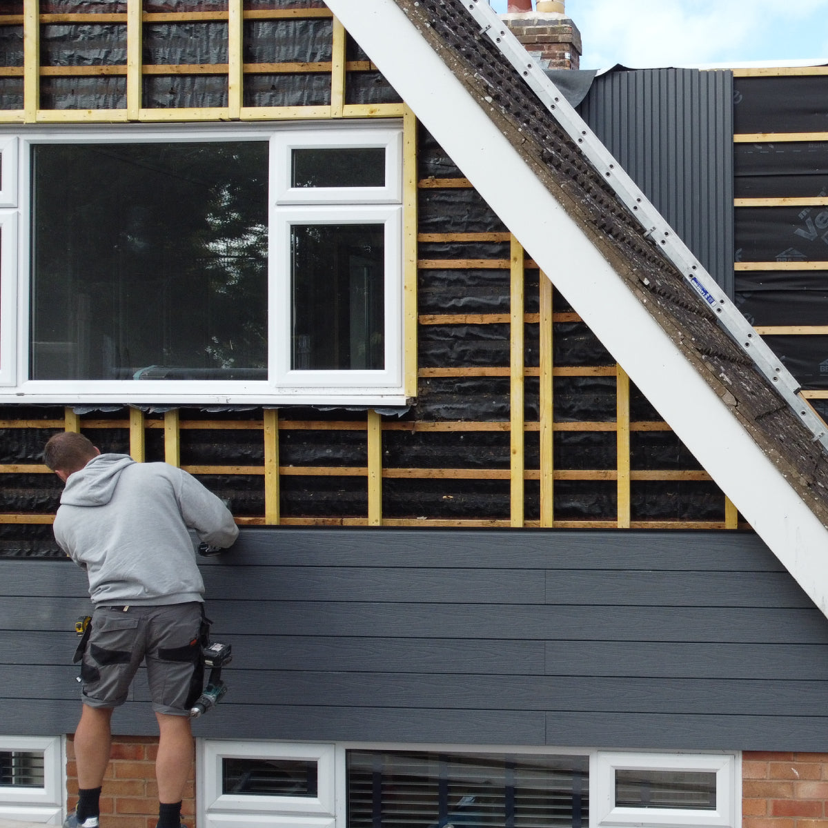 person installing composite siding on a house with a ladder and tools