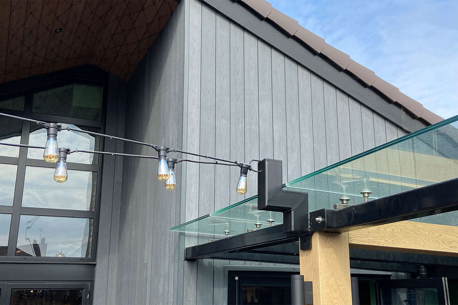 modern building exterior with grey deluxe composite cladding, glass canopy and decorative lights