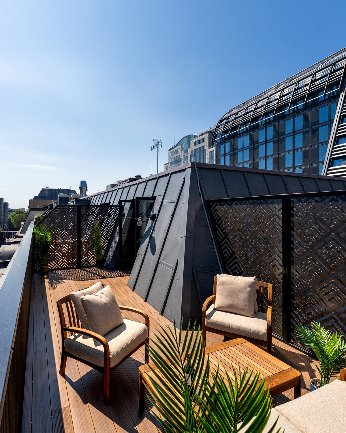 outdoor seating area on rooftop terrace decking with chairs, table, and plants under a clear blue sky