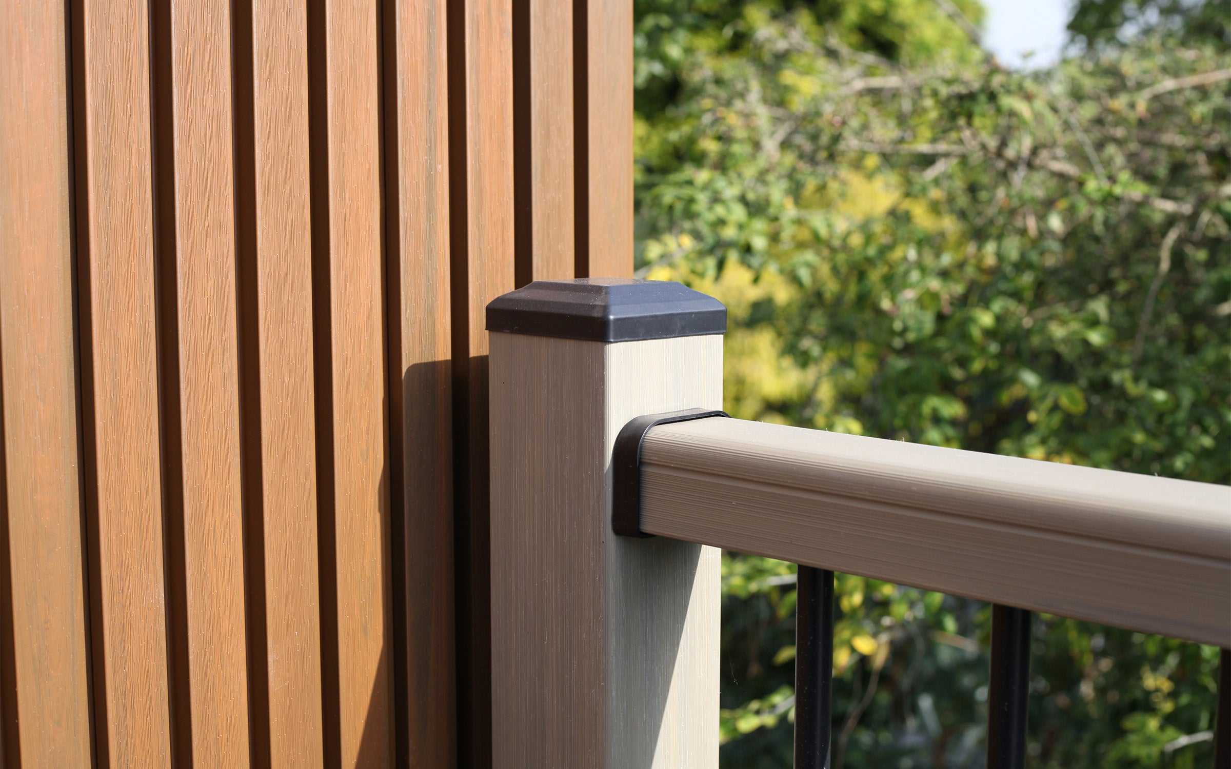 slat panel wall with a composite railing and greenery in the background