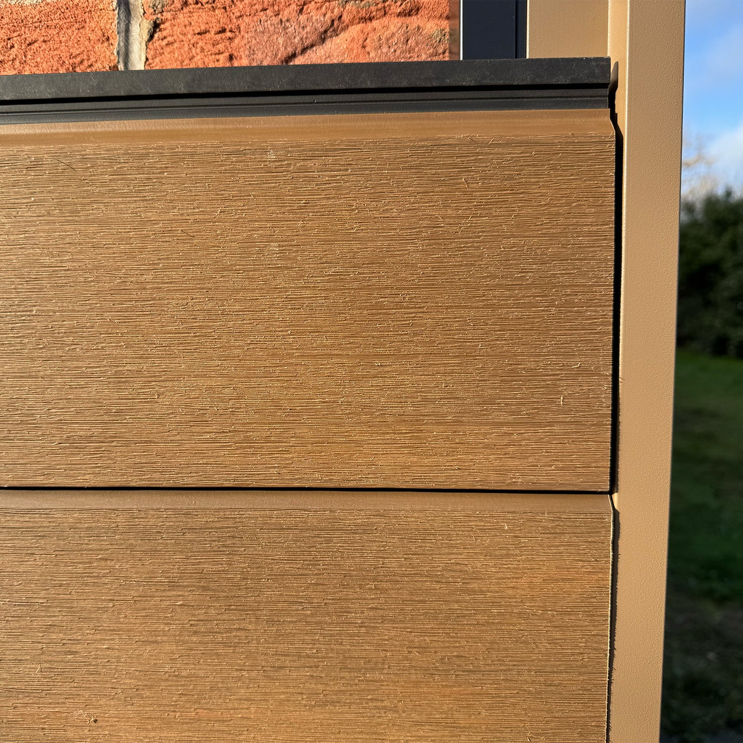 close-up of composite cladding paneling on a building exterior with a brick wall and blue sky in the background