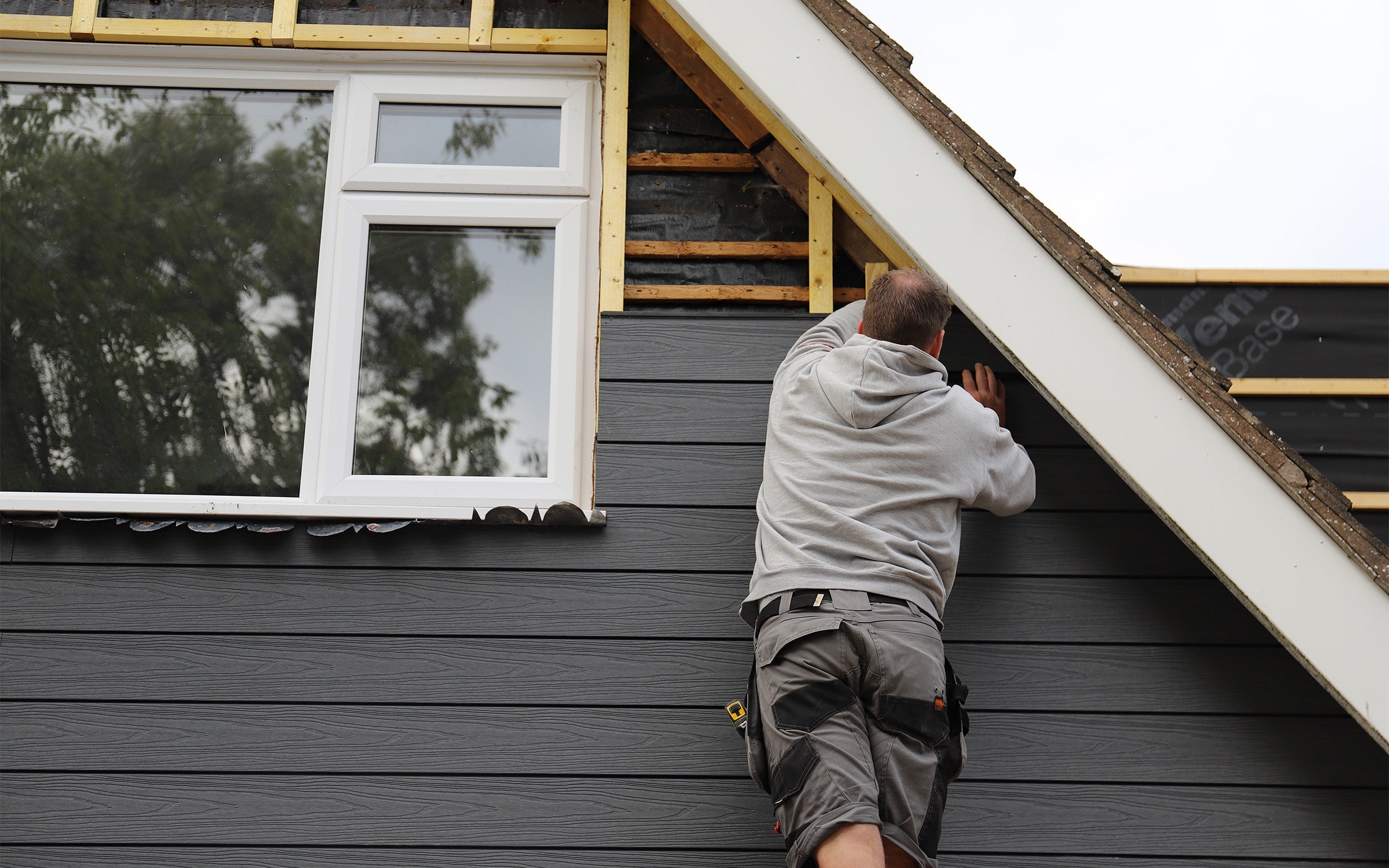 person climbing a ladder on a house exterior installing composite cladding