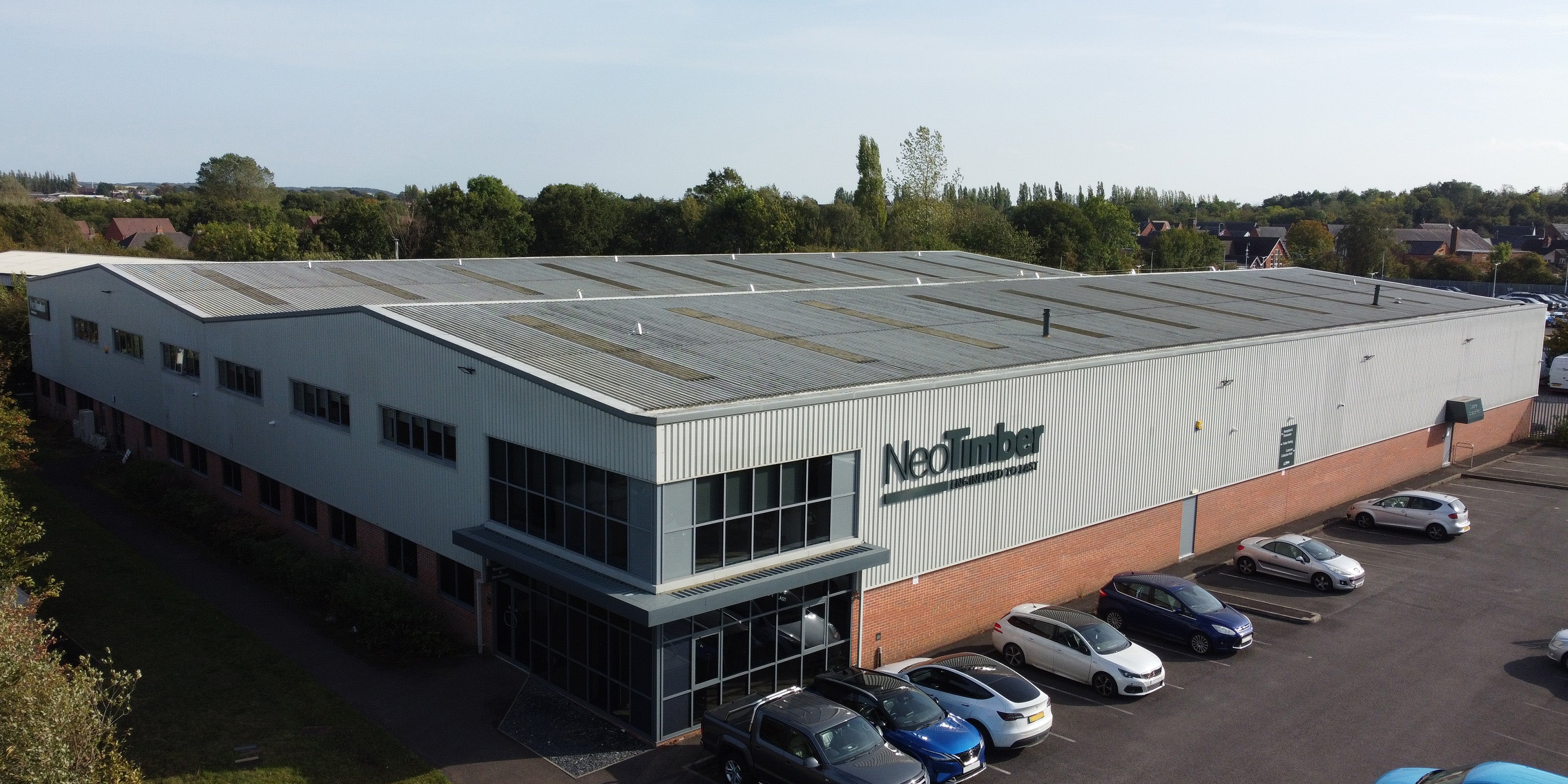 aerial view of a large industrial building with 'NeoTimber' branding, surrounded by parked cars and greenery