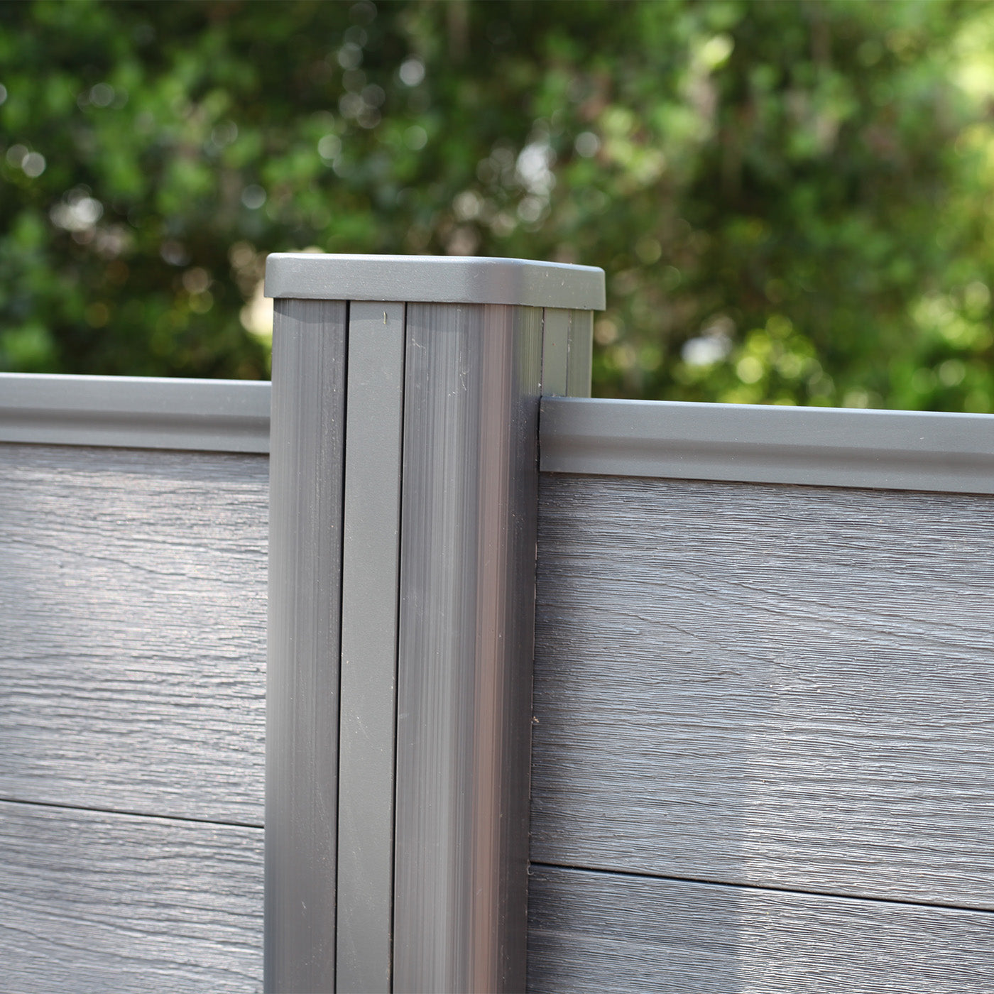 close-up of grey composite fence panels and post with soft-focus garden greenery in the background