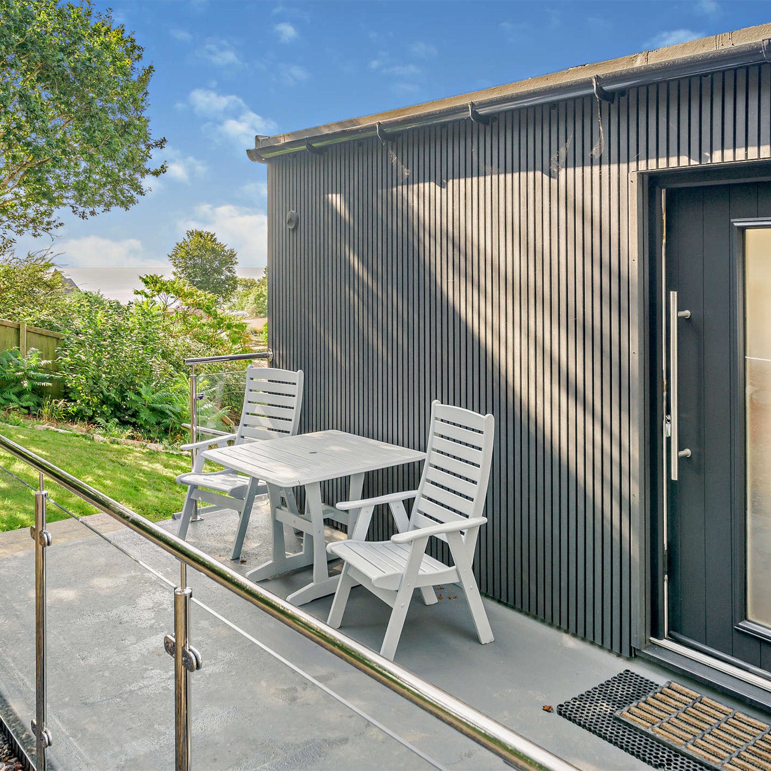 outdoor seating area with a small table and chairs on a patio next to a slatted composite clad building