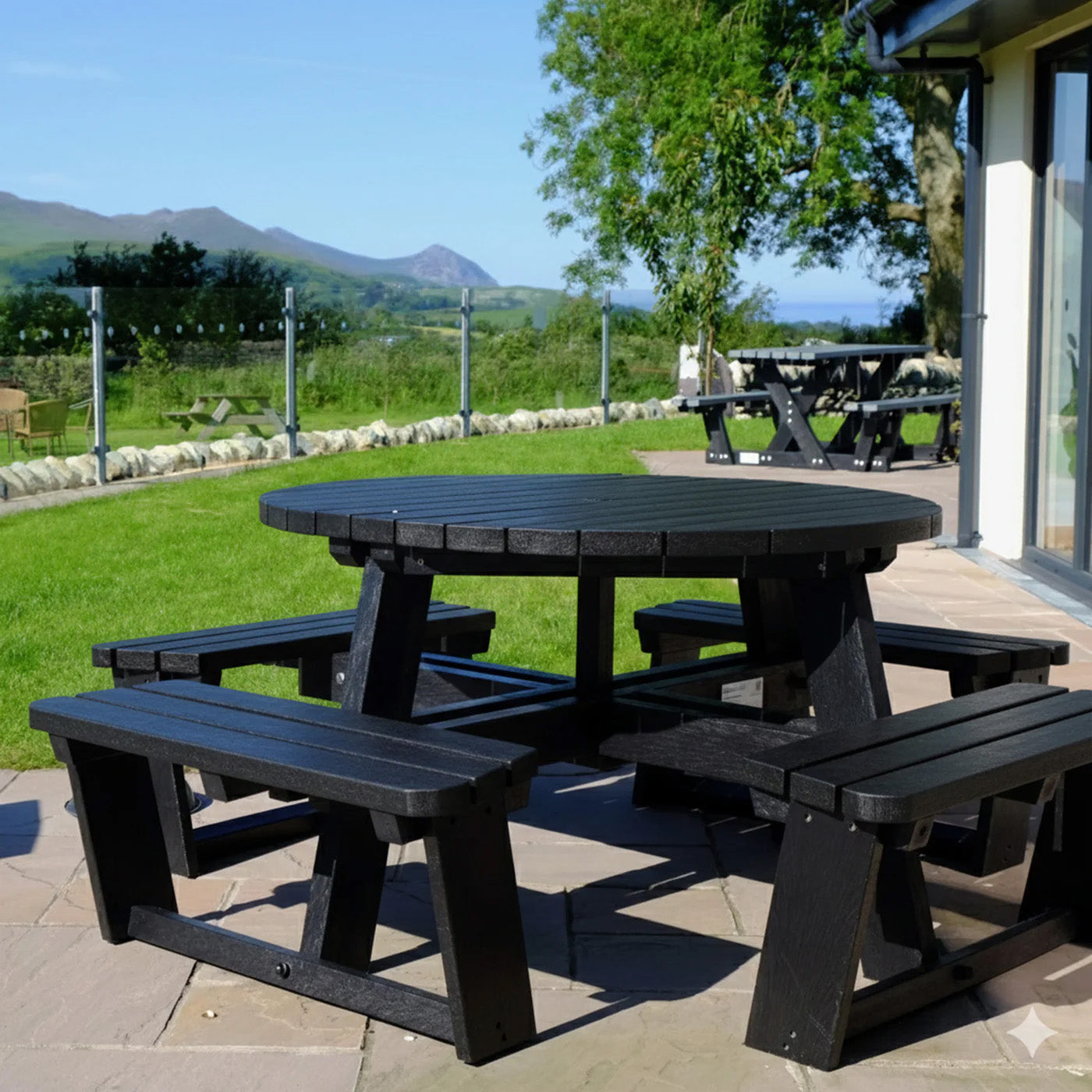 round black recycled plastic picnic table with benches on a patio area with a scenic background