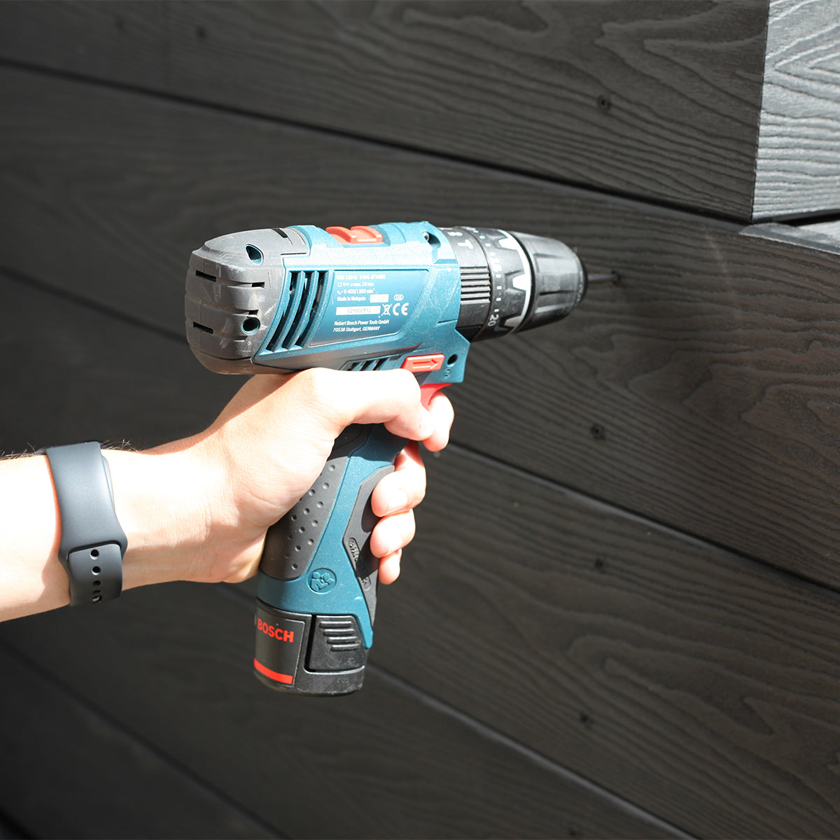 hand holding a Bosch power drill against a composite wall cladding background