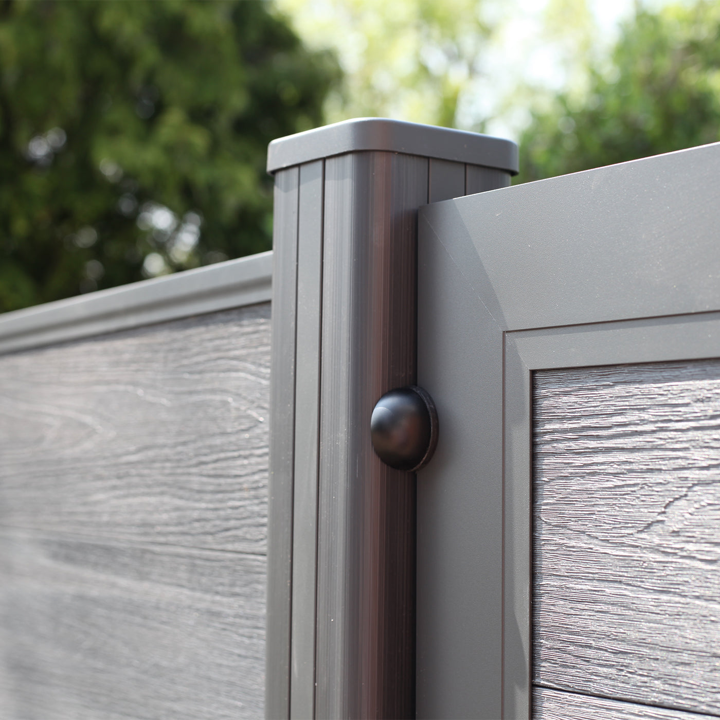 close-up of grey composite fence panel and post with blurred green background