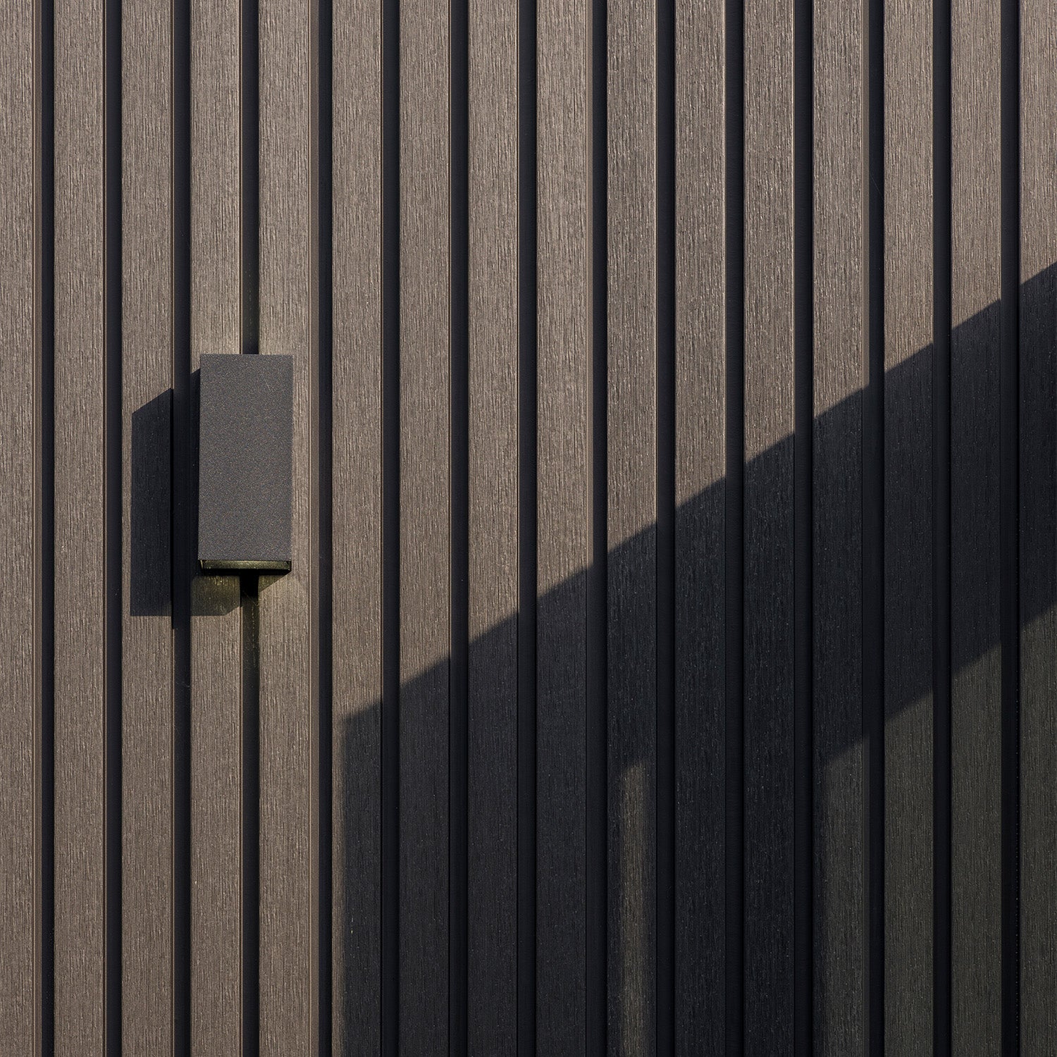 dark rectangular light fixture mounted on textured brown composite cladding wall