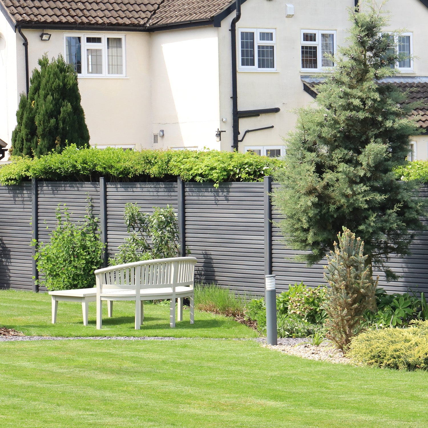 garden with a grey composite fence, grass, and a house in the background