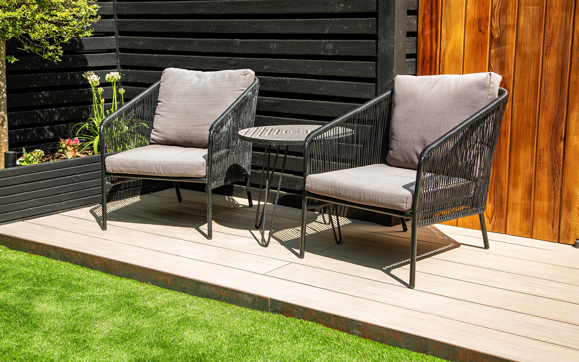 two wicker chairs with grey cushions on a composite deck against a wall
