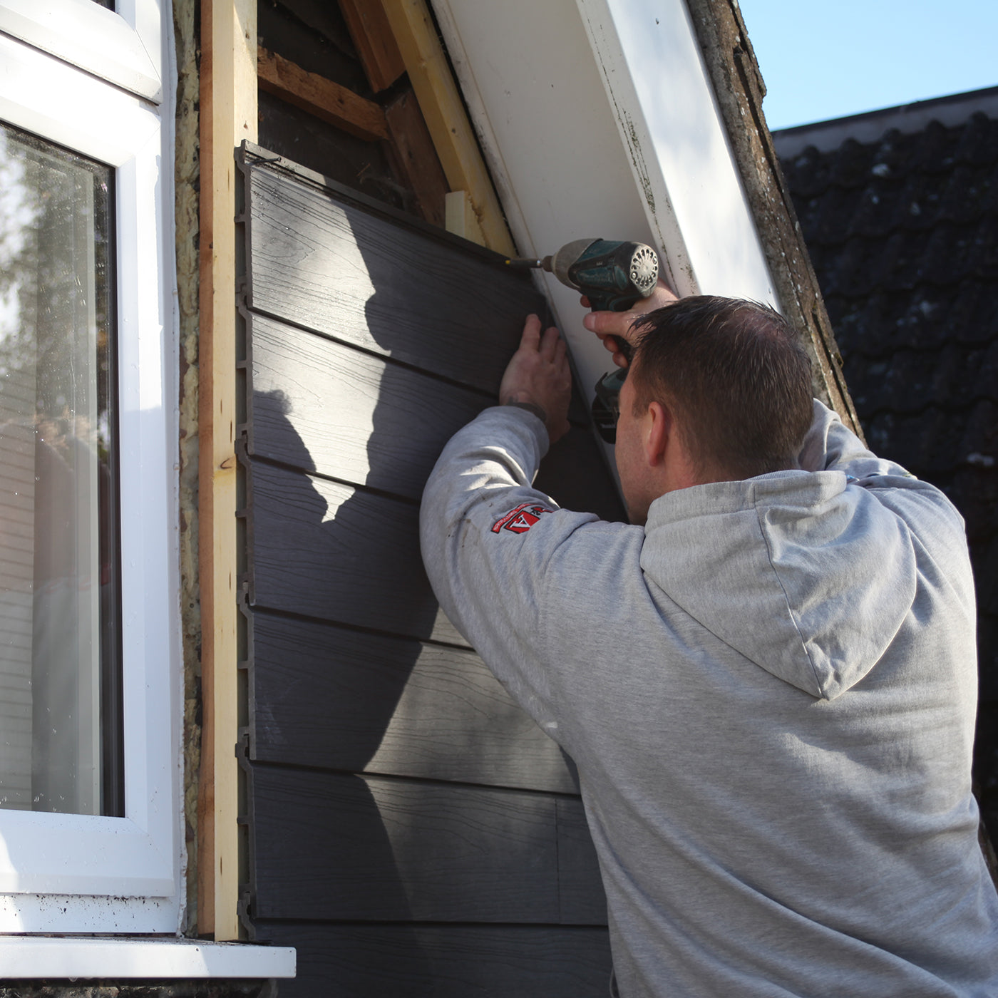 a tradesperson installing grey woodgrain composite cladding on a house exterior, representing the neotimber approved installer program
