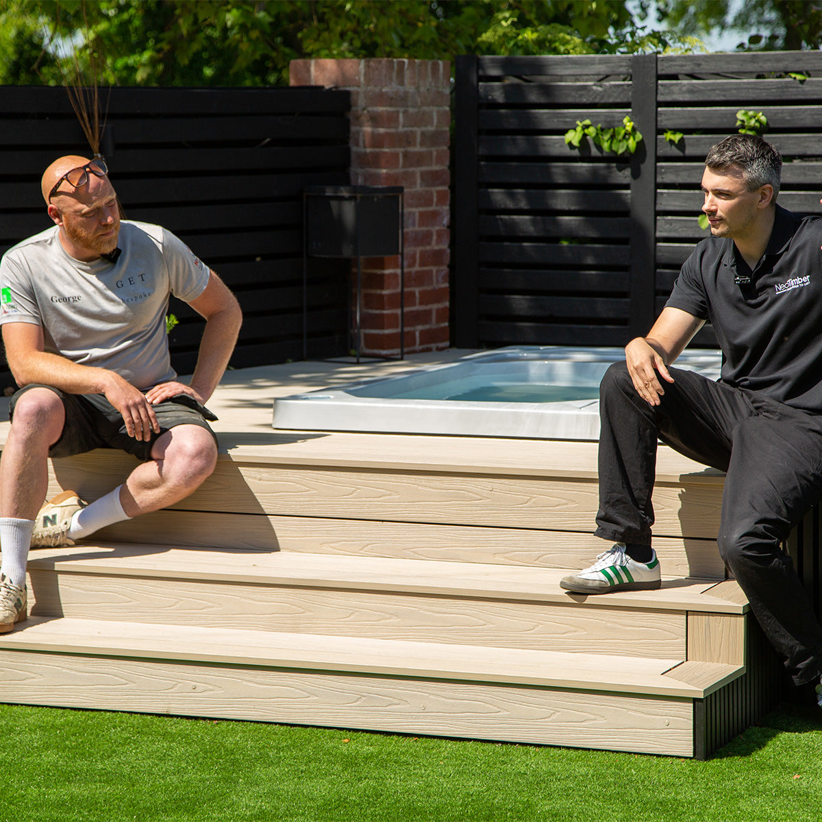 Two men sitting on composite decking steps in a backyard with a hot tub