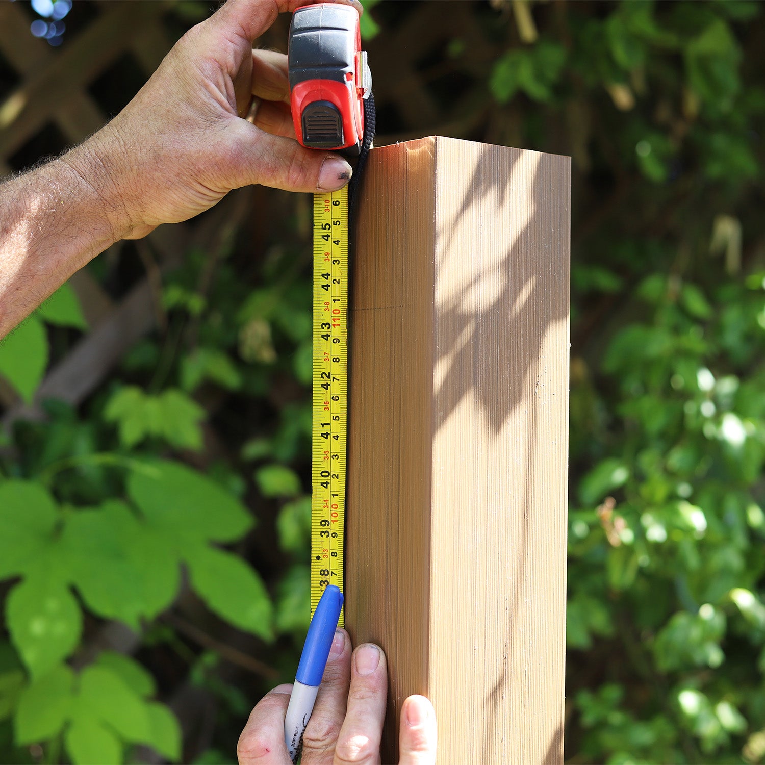 hand measuring a neotimber composite balustrade post with a tape measure against a green outdoor background