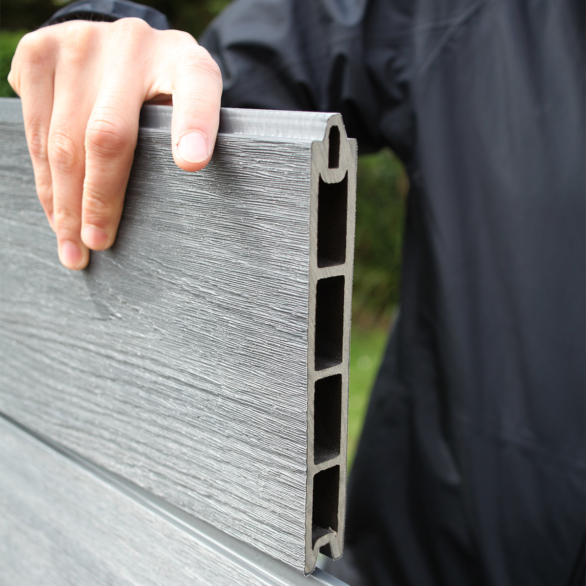 person holding a composite fence board panel with a textured surface