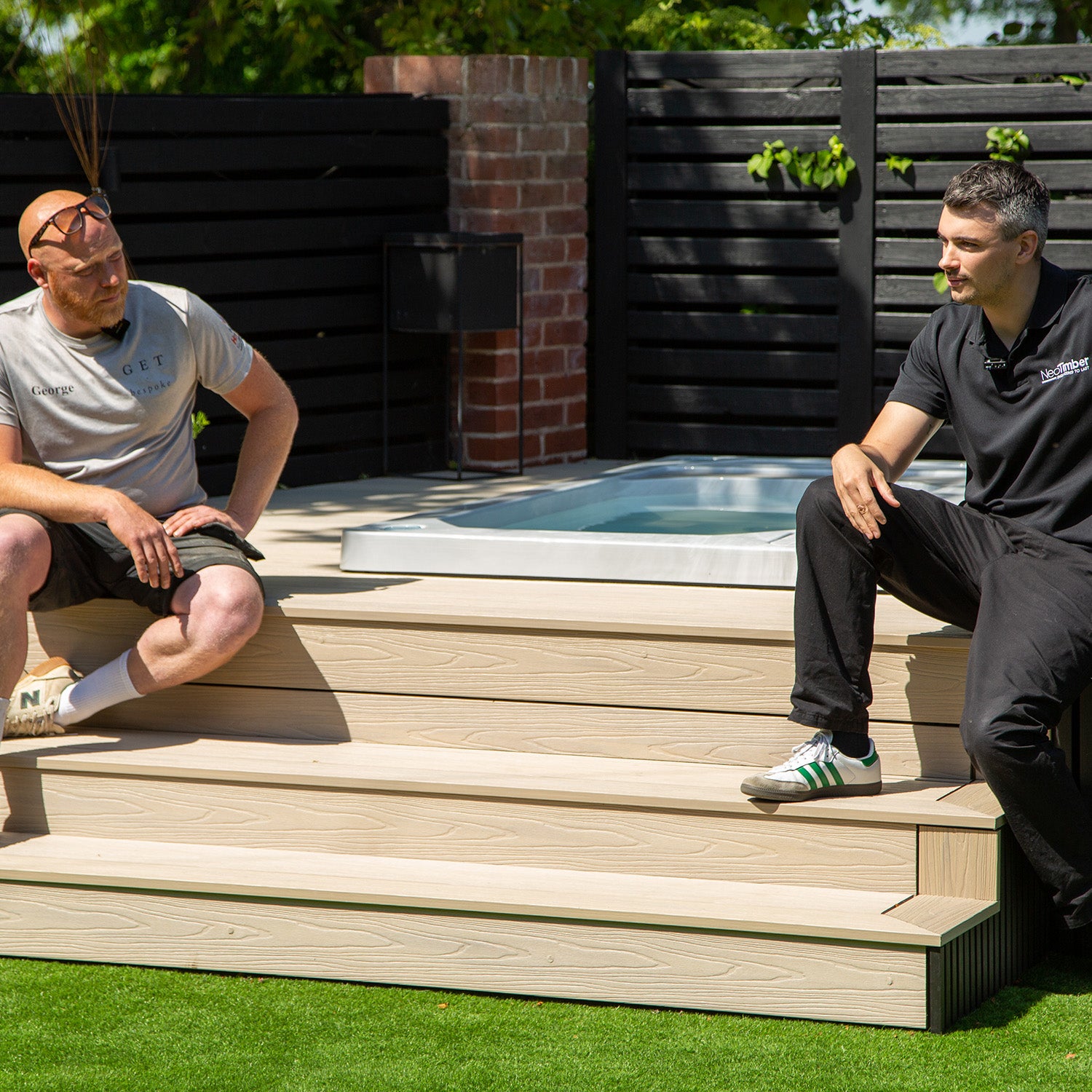 two men sitting on composite decking steps by a hot tub in a backyard setting