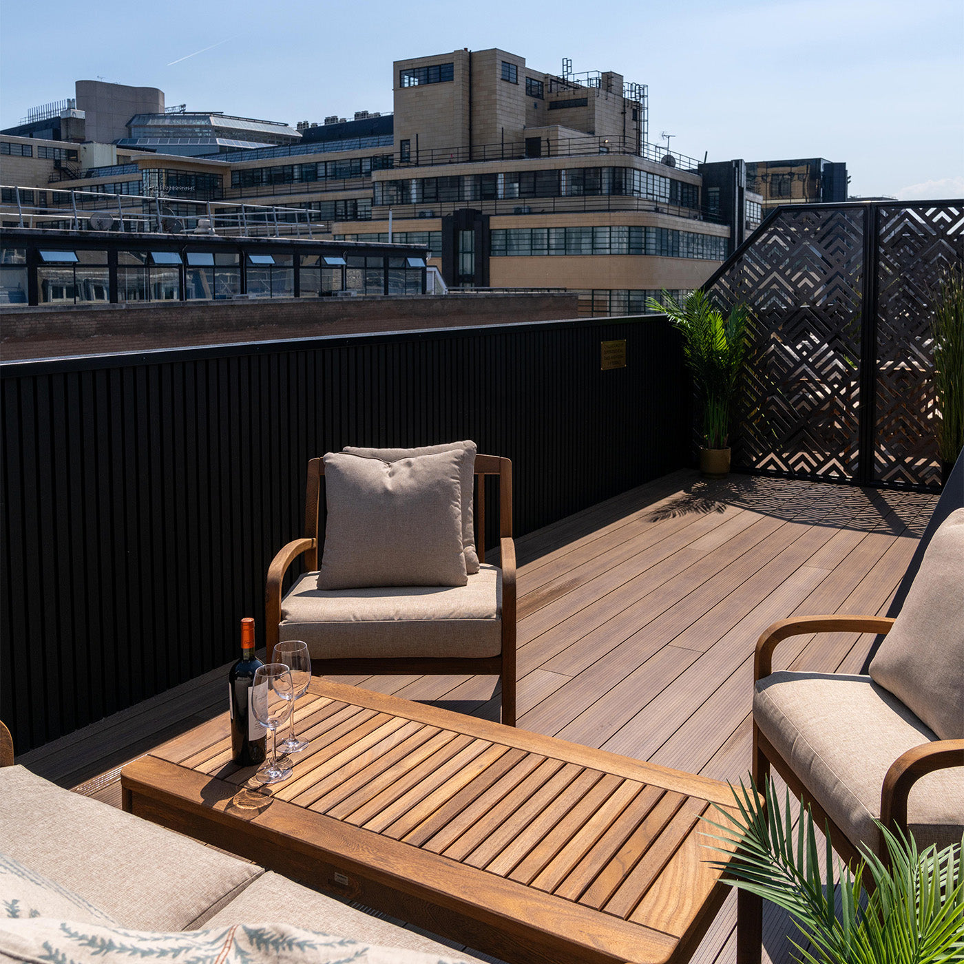 outdoor seating area on a rooftop with aluminium decking, wooden table and chairs, cityscape in the background.