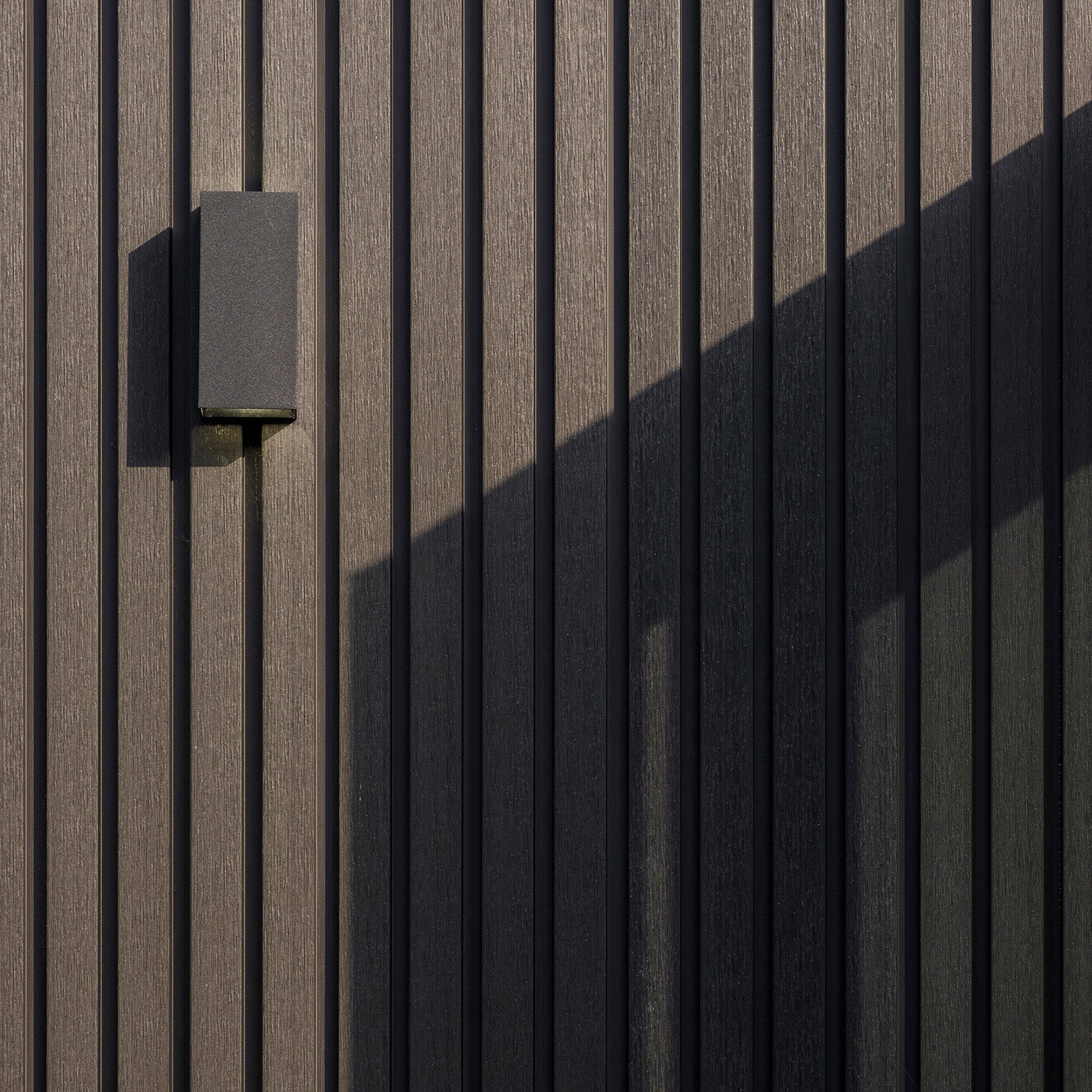 modern outdoor wall light fixture on a slatted composite cladding panel wall