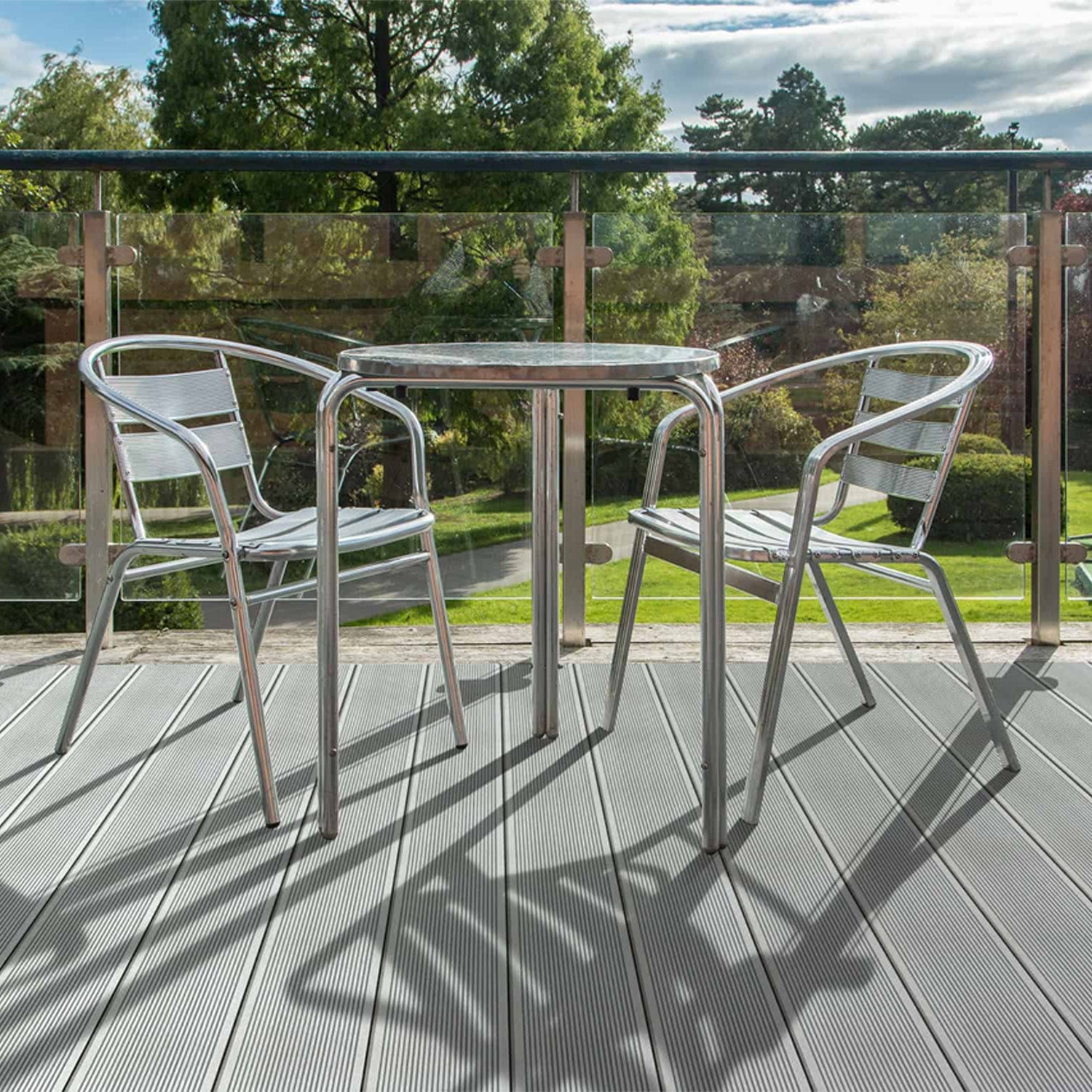 outdoor patio set with a table and two chairs on a grey composite deck with a garden view