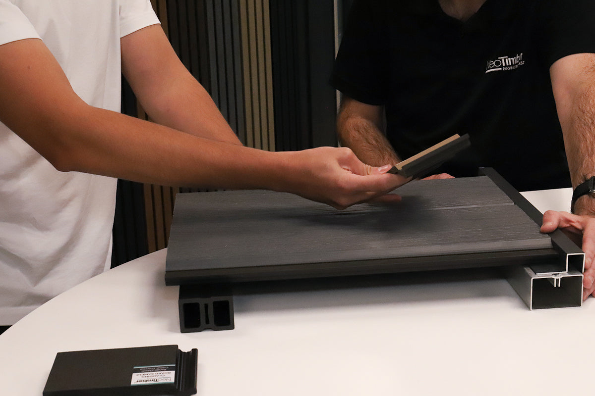 two people examining a decking subframe sample on a white table