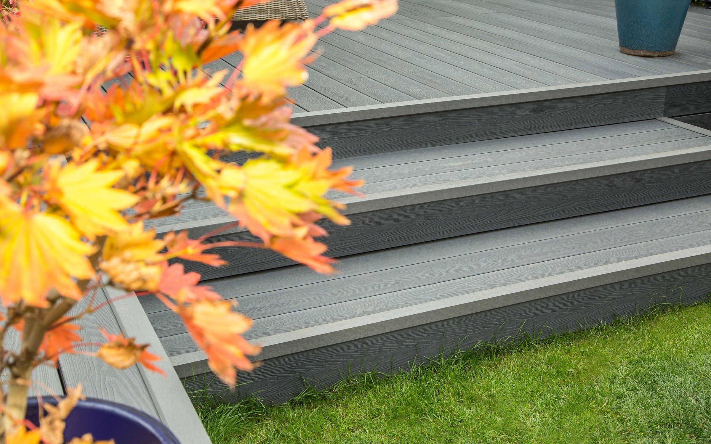 grey composite decking steps leading to a deck with autumn leaves on the left