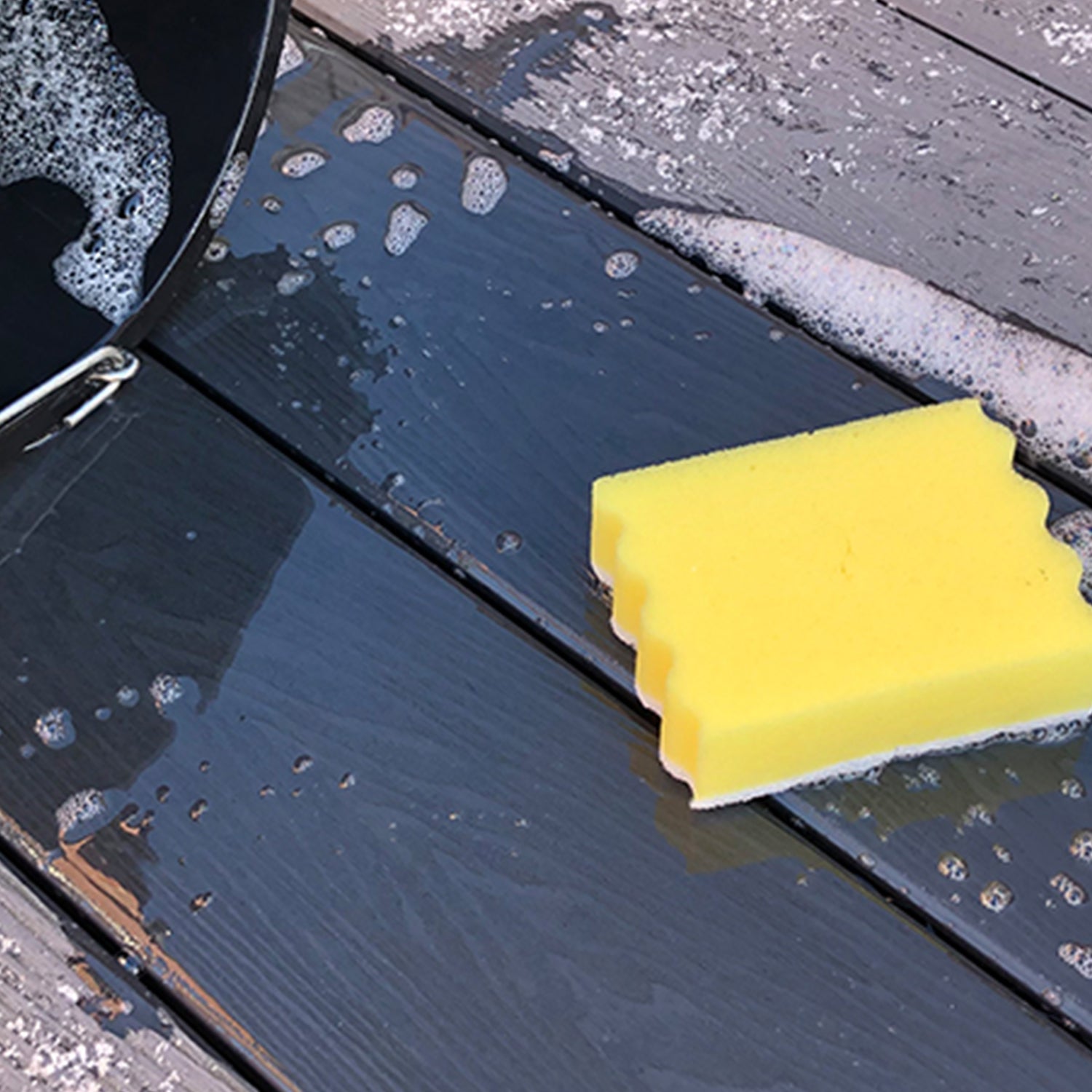 yellow sponge cleaning a composite deck surface with soapy water