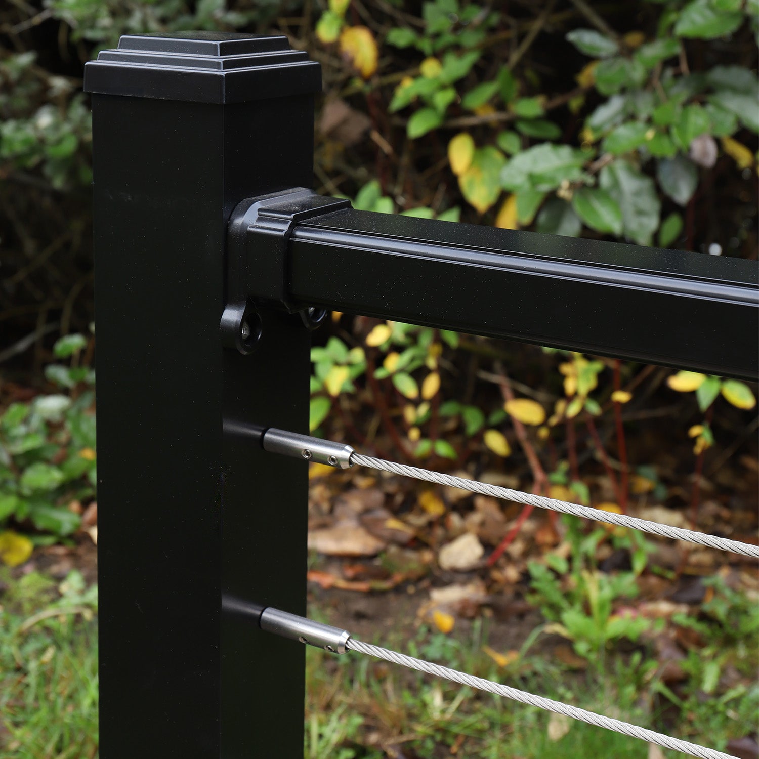 close-up of a black aluminium wire balustrade featuring cable infills and a post in a landscaped garden setting