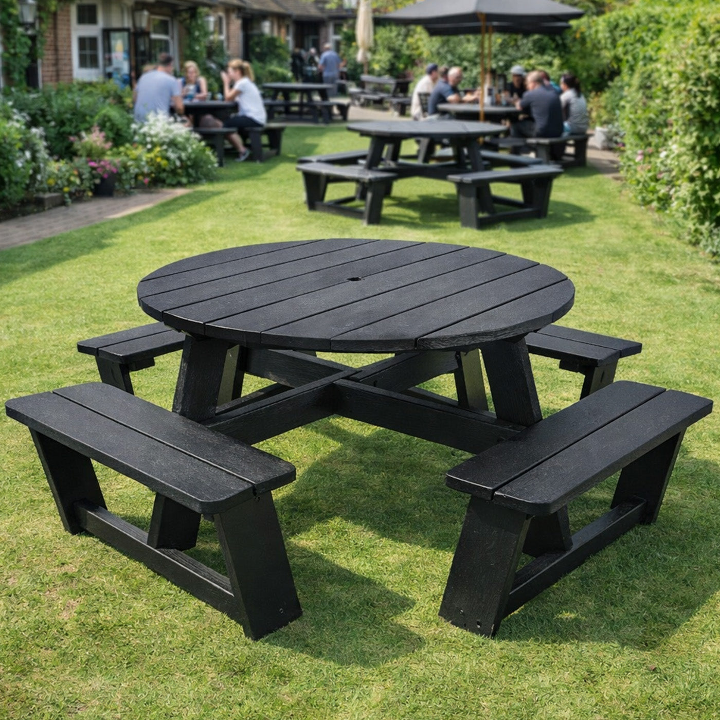 black recycled plastic round picnic table with benches on a grassy area, surrounded by other tables and people in an outdoor setting