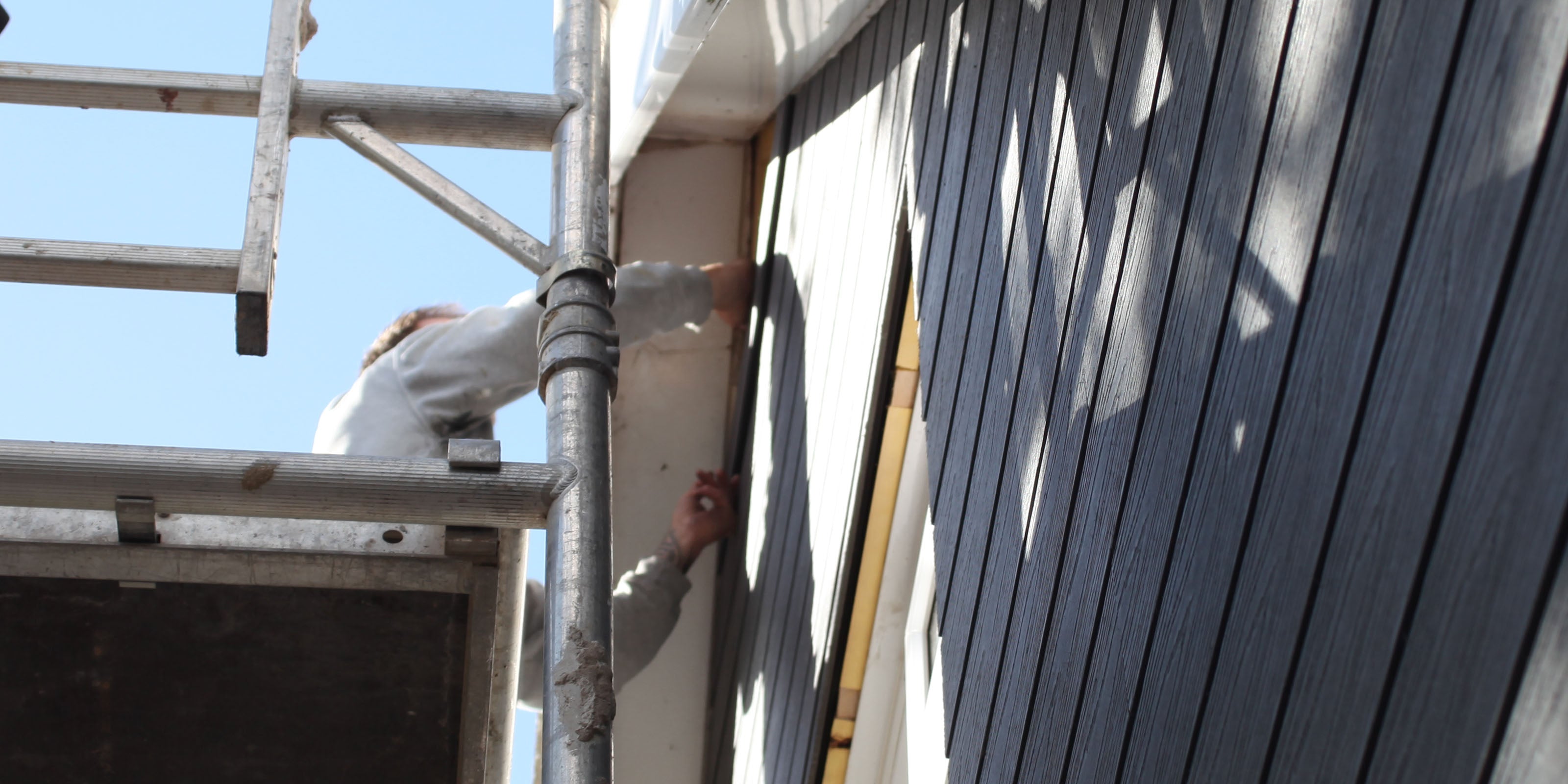 installer fitting composite cladding on building with scaffolding in background