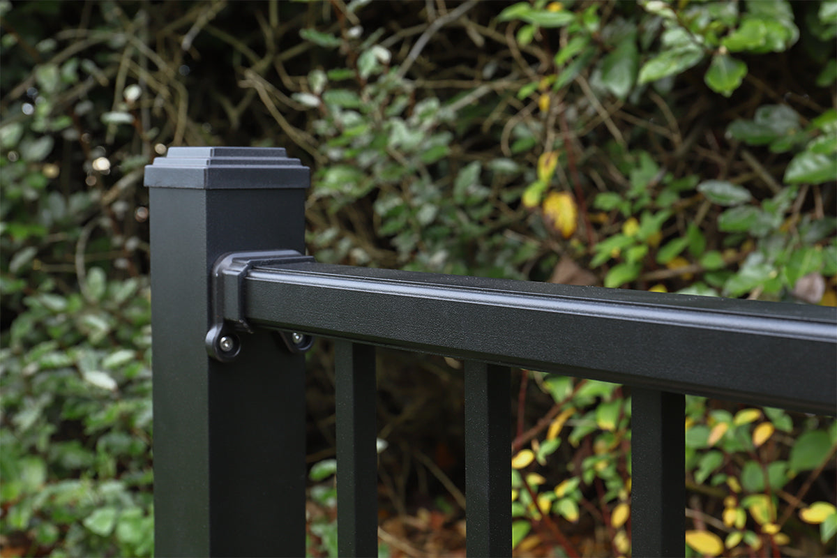 close-up of a black metal hand railing with green foliage in the background
