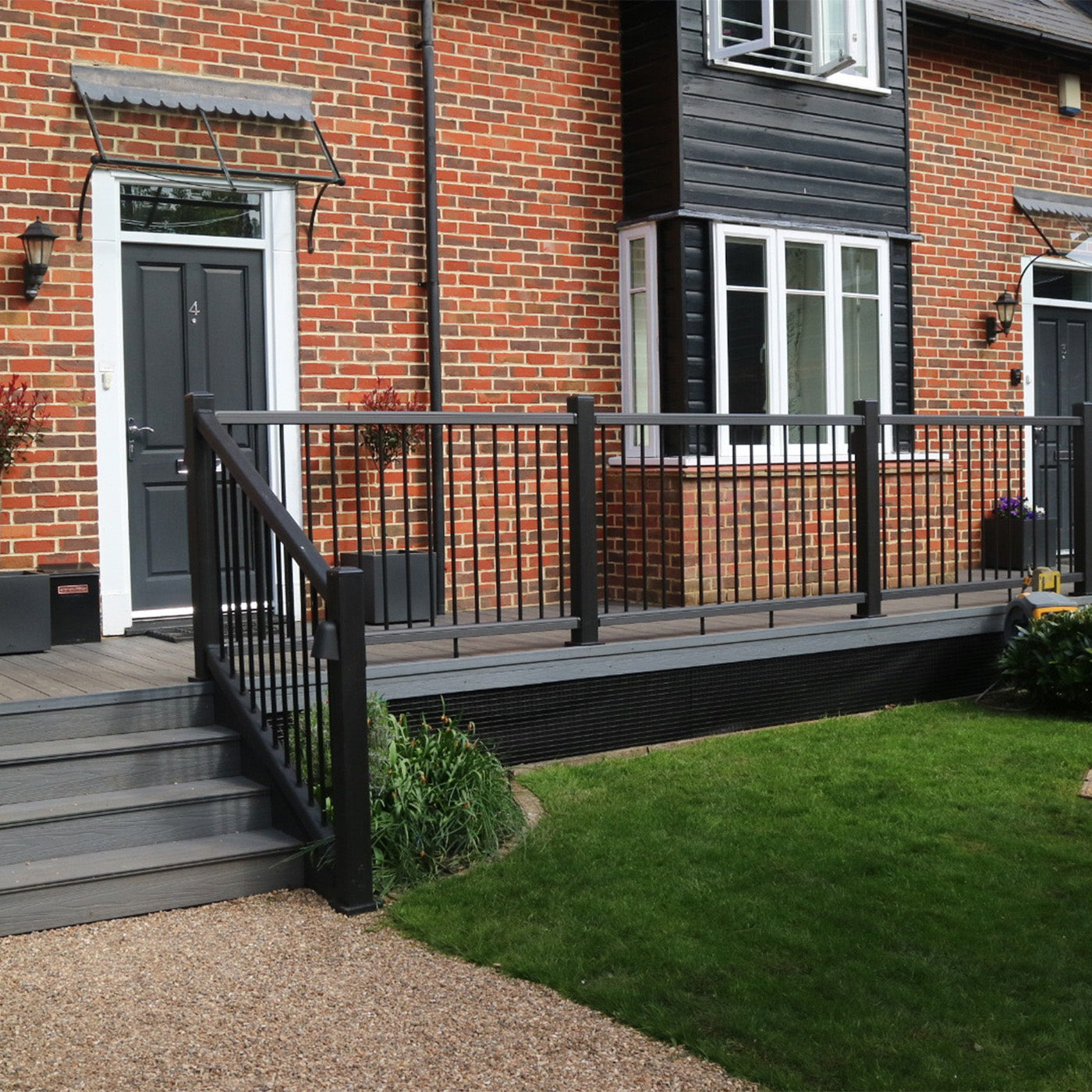 home exterior with a neotimber black composite deck and railing, green lawn, and brick wall