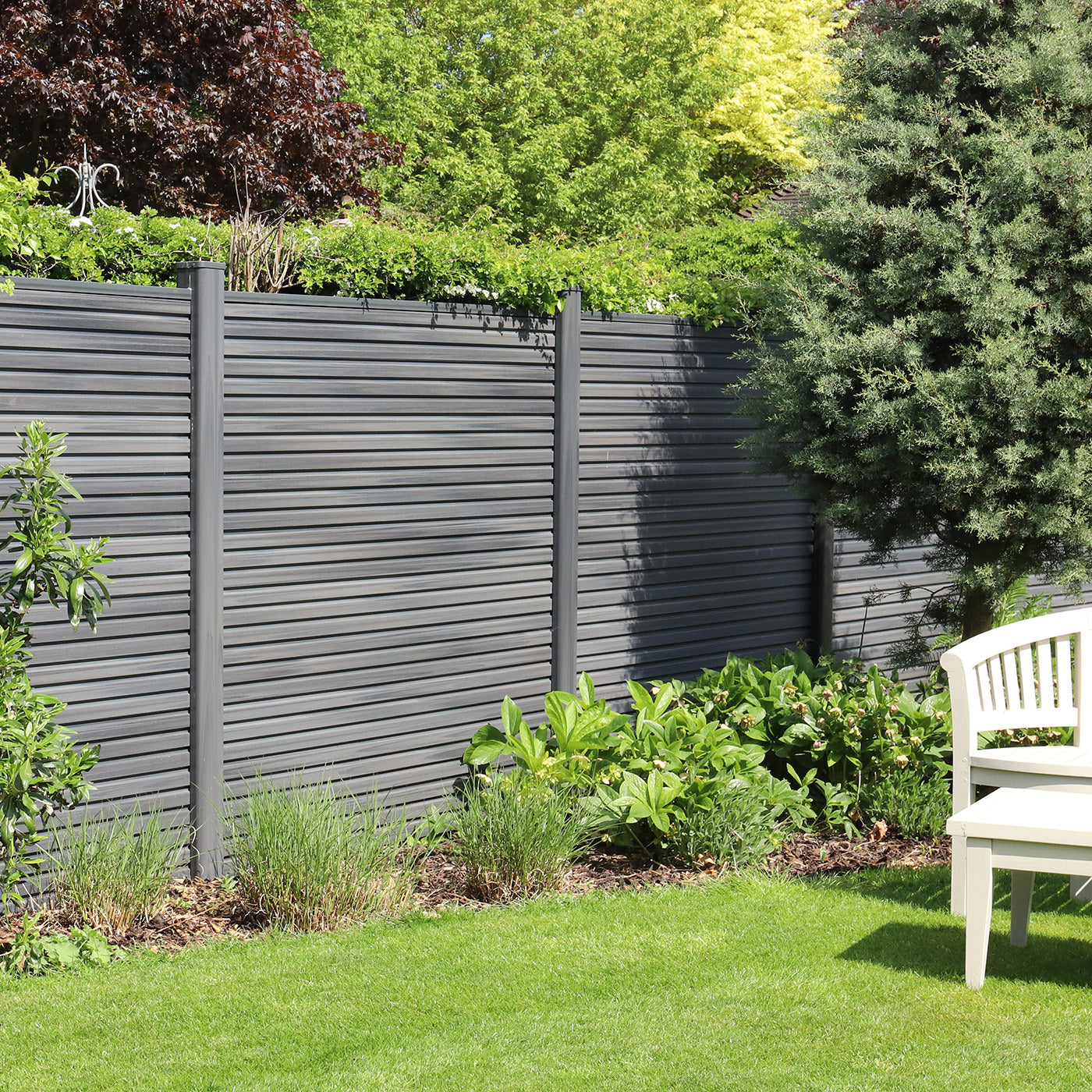 grey composite fence with greenery and a white bench in a garden setting