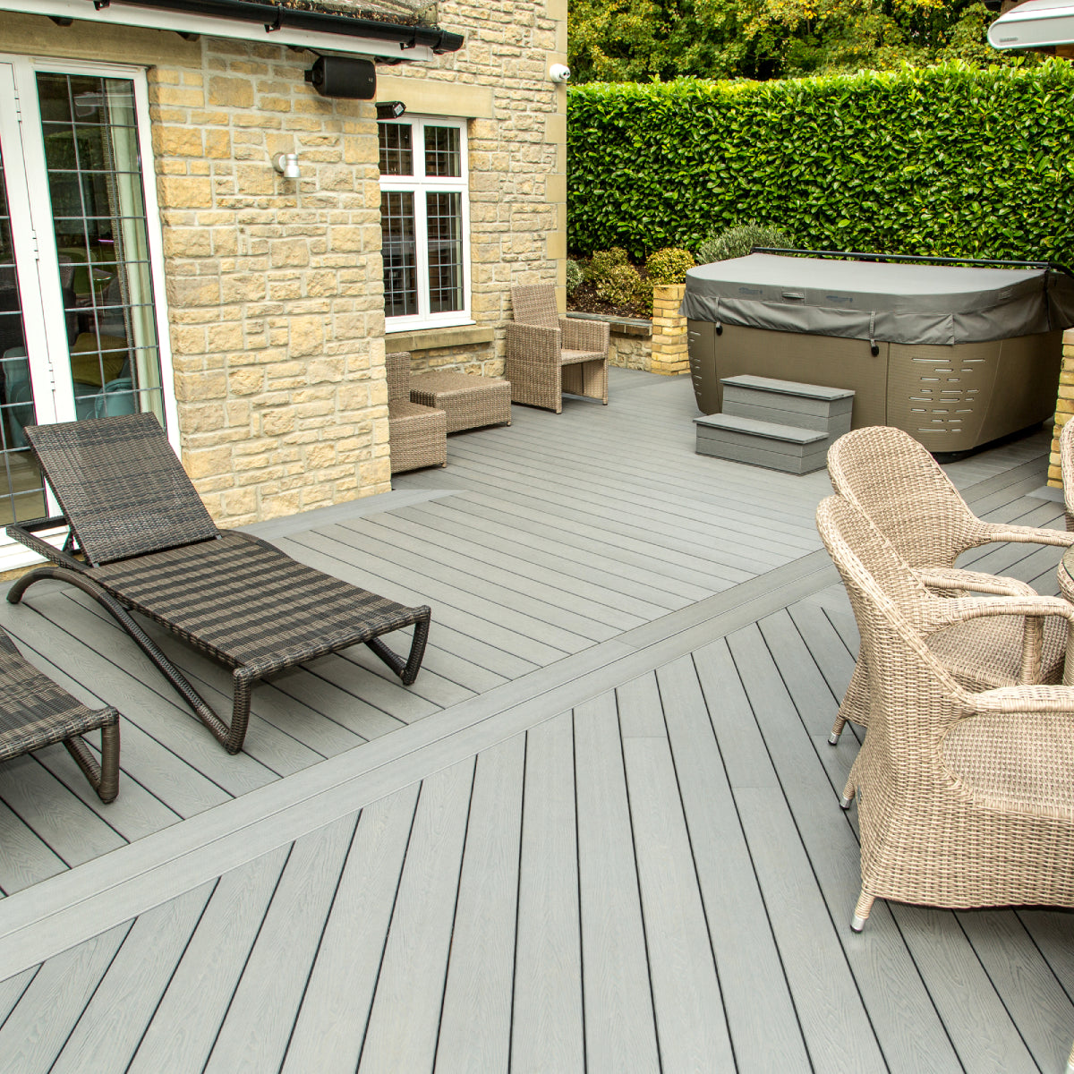 outdoor patio area with deck chairs, table, and hot tub cover on a grey composite deck