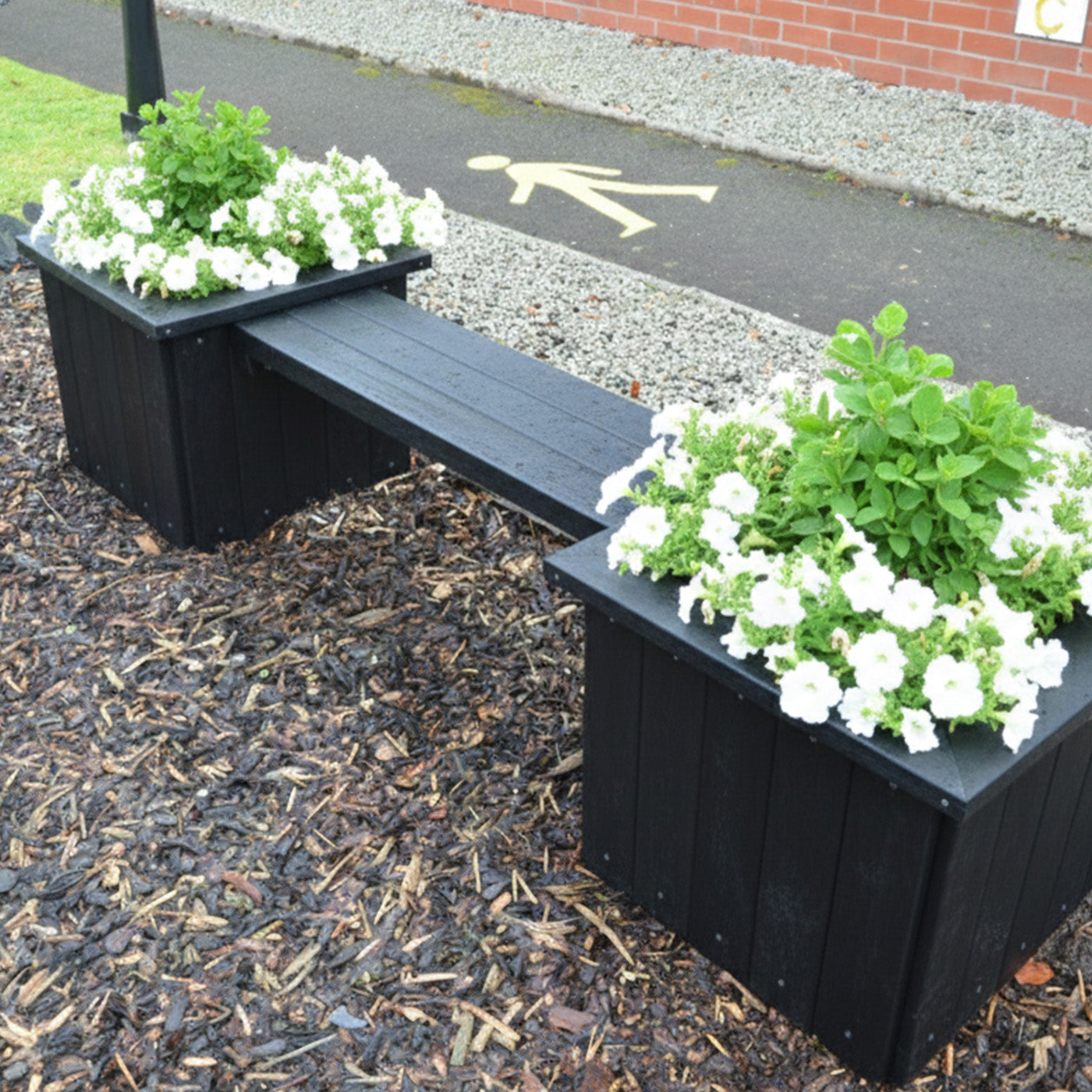 recycled plastic bench with planters filled with white flowers and green plants on a mulched area