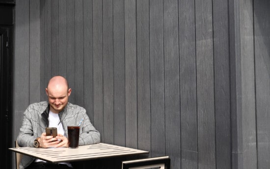 man sat on phone in front of composite cladding wall